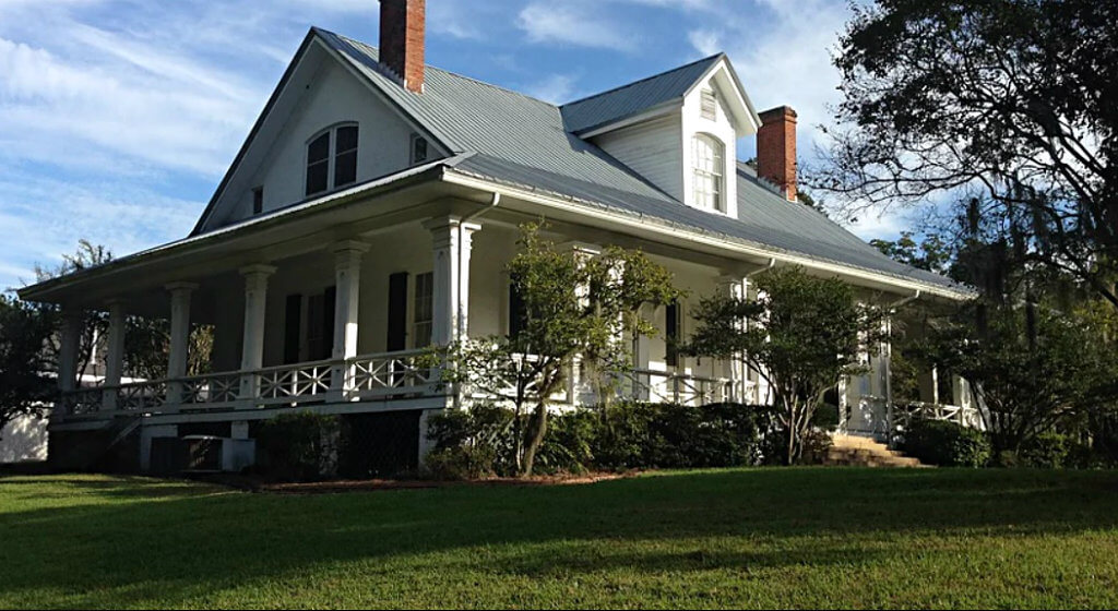 exterior view of white plantation style home with centered second floor dormer taken from green lawn
