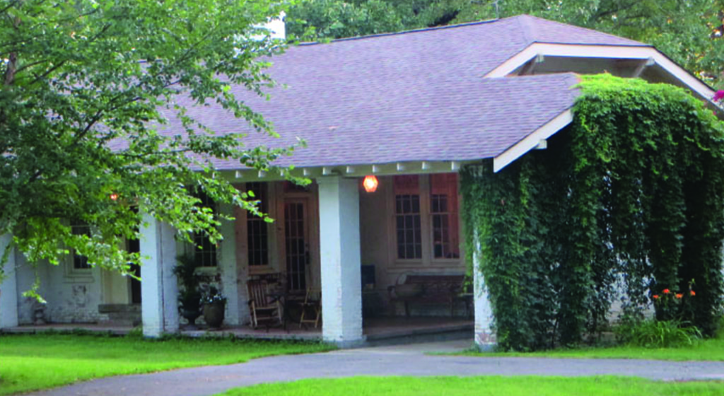 white house with white posts in front with green vines growing on side of house